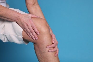 Photo of Woman suffering from pain in her knee on light blue background, closeup. Space for text