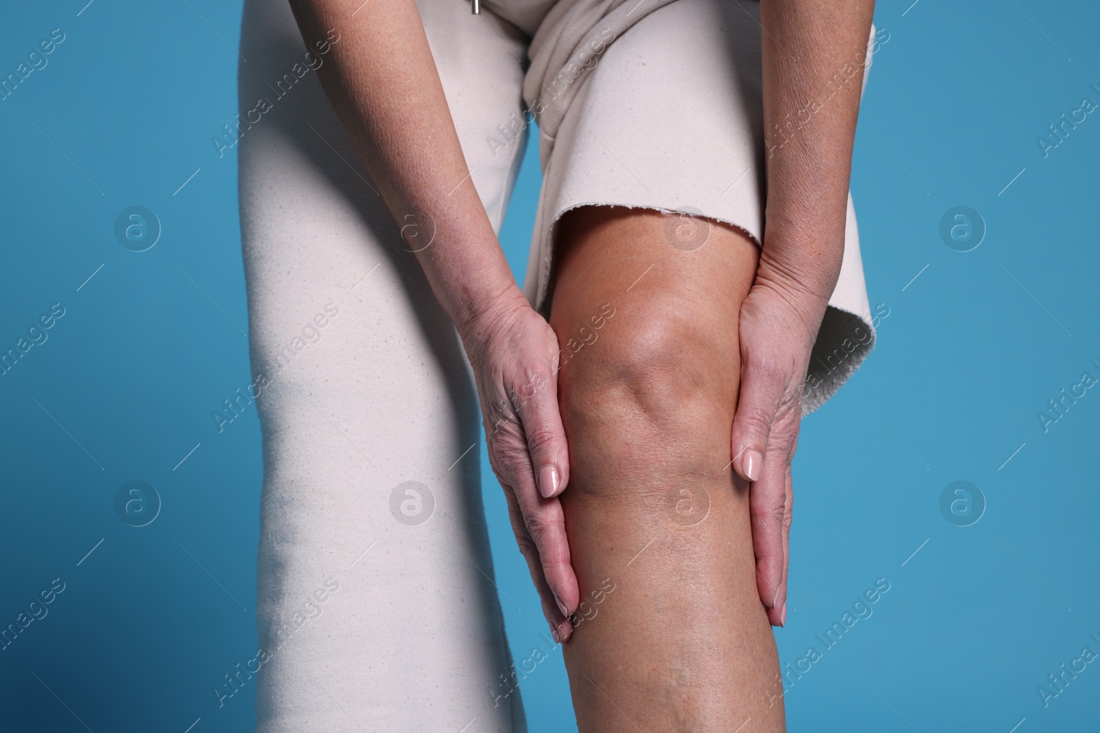 Photo of Woman suffering from pain in her knee on light blue background, closeup