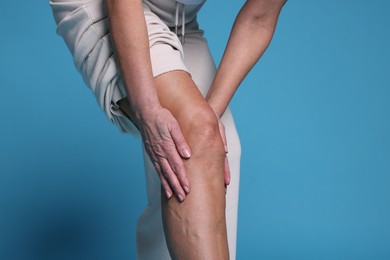 Photo of Woman suffering from pain in her knee on light blue background, closeup