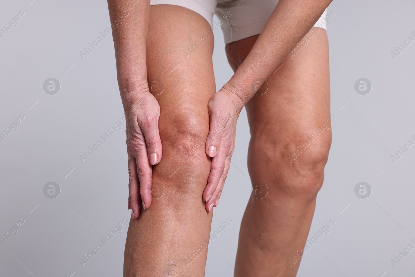 Photo of Woman suffering from pain in her knee on light grey background, closeup