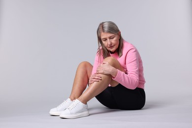 Photo of Senior woman suffering from knee pain on light grey background