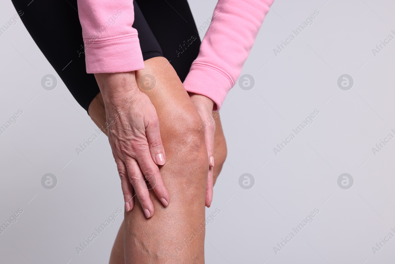 Photo of Woman suffering from pain in her knee on light grey background, closeup. Space for text