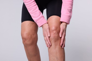 Photo of Woman suffering from pain in her knee on light grey background, closeup