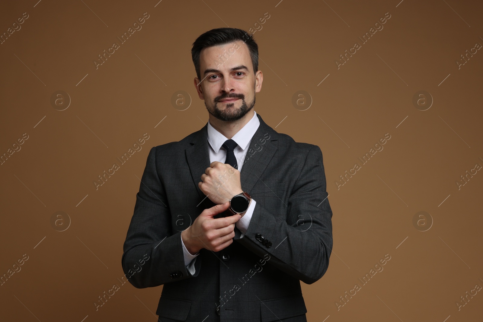 Photo of Confident man in classic suit with stylish watch on brown background