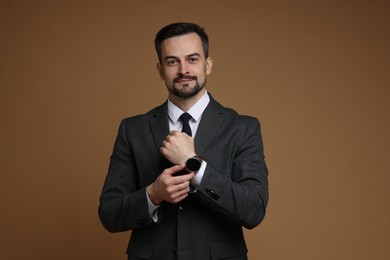 Photo of Confident man in classic suit with stylish watch on brown background