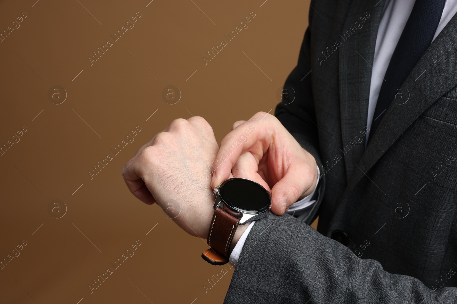 Photo of Man in classic suit checking time on brown background, closeup. Space for text