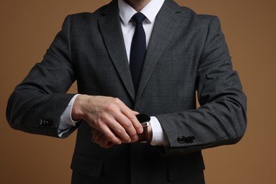 Photo of Man in classic suit checking time on brown background, closeup