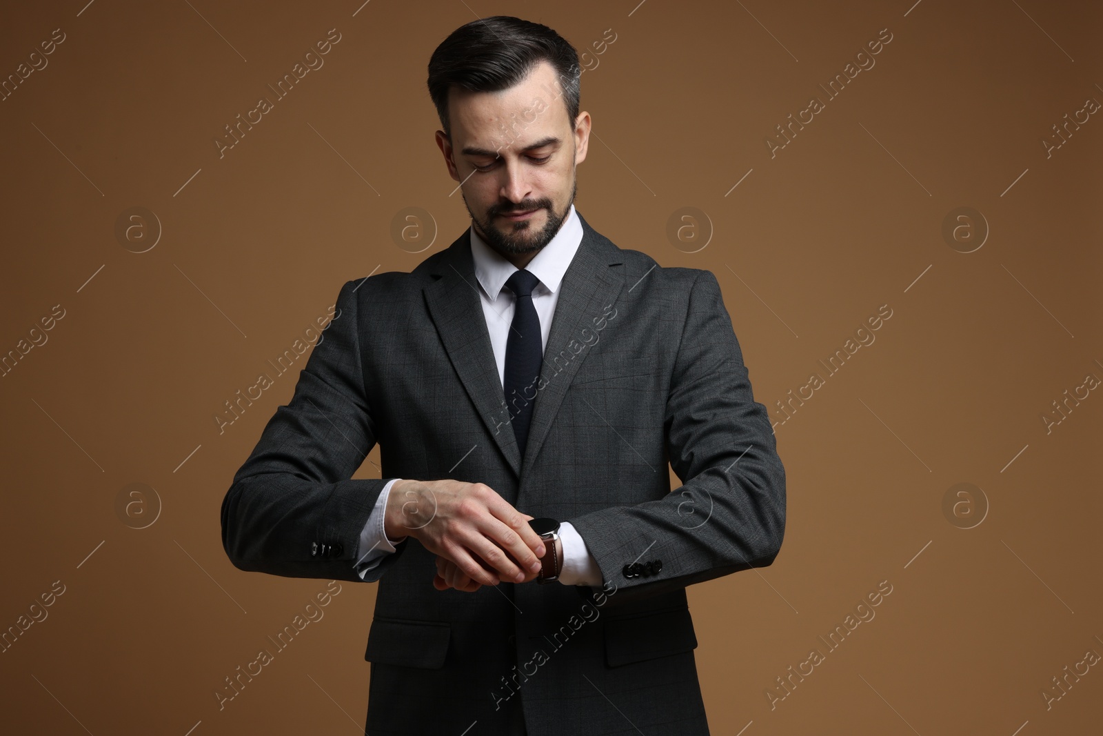 Photo of Man in classic suit checking time on brown background