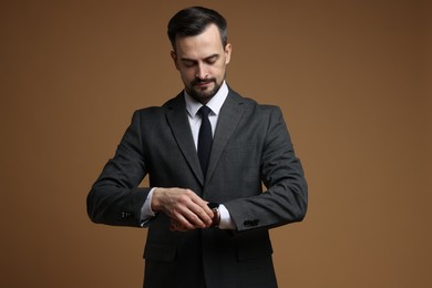 Photo of Man in classic suit checking time on brown background