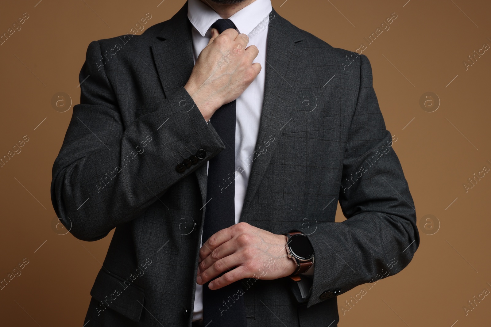 Photo of Man in classic suit straightening tie on brown background, closeup