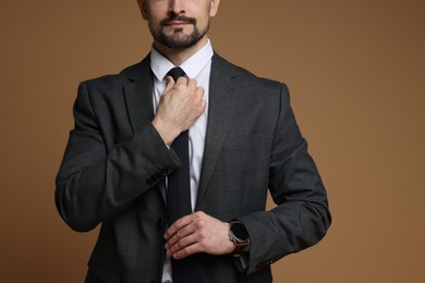 Photo of Man in classic suit straightening tie on brown background, closeup