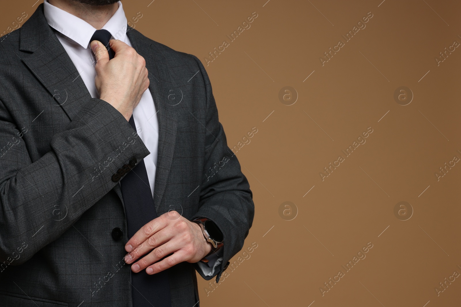 Photo of Man in classic suit straightening tie on brown background, closeup. Space for text