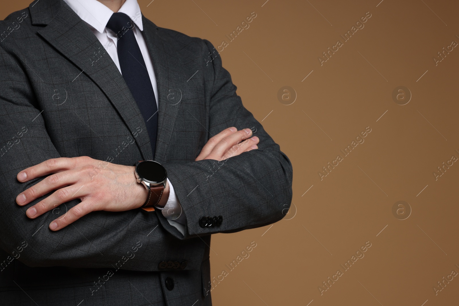 Photo of Man in classic suit with stylish watch on brown background, closeup. Space for text