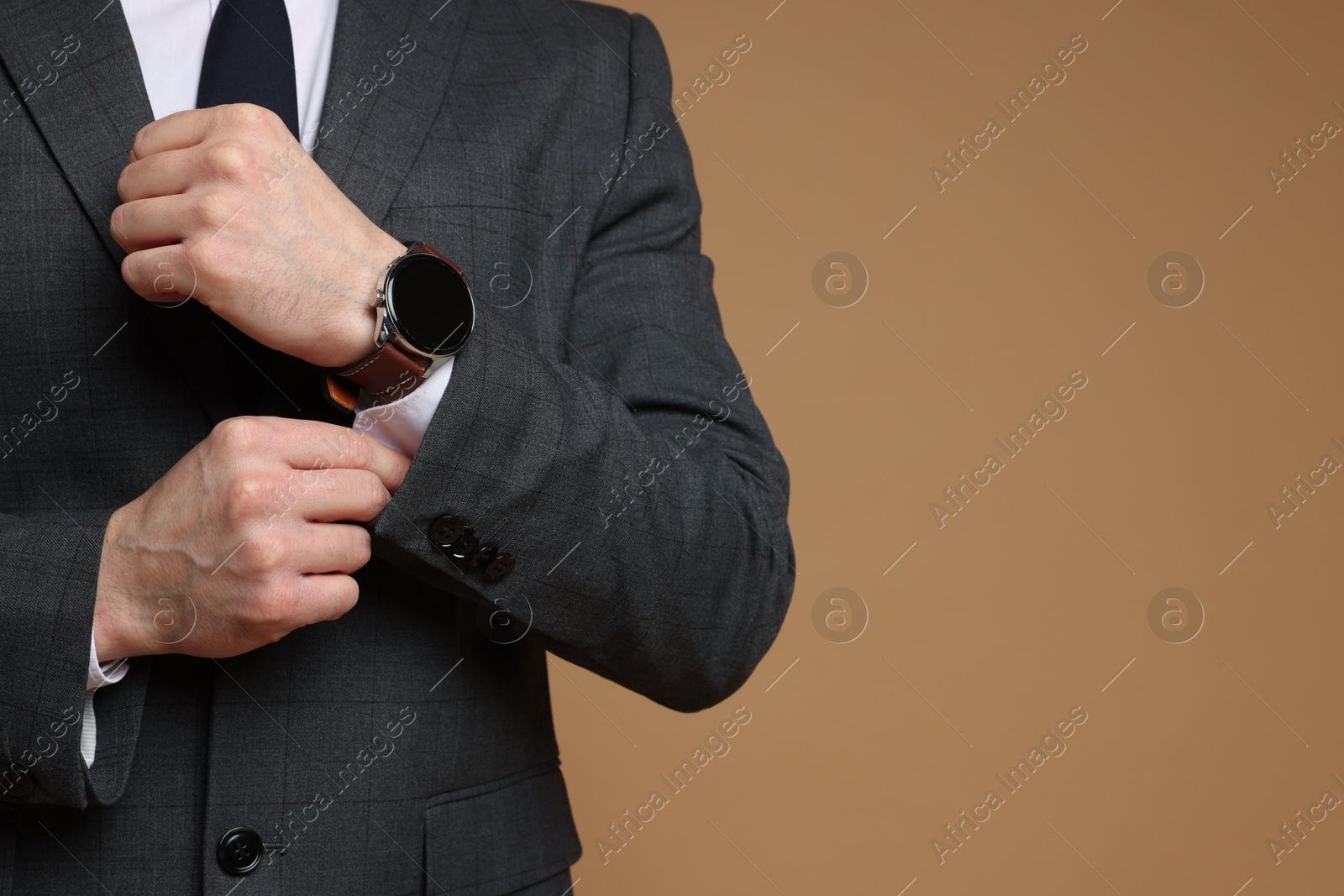 Photo of Man in classic suit with stylish watch on brown background, closeup. Space for text