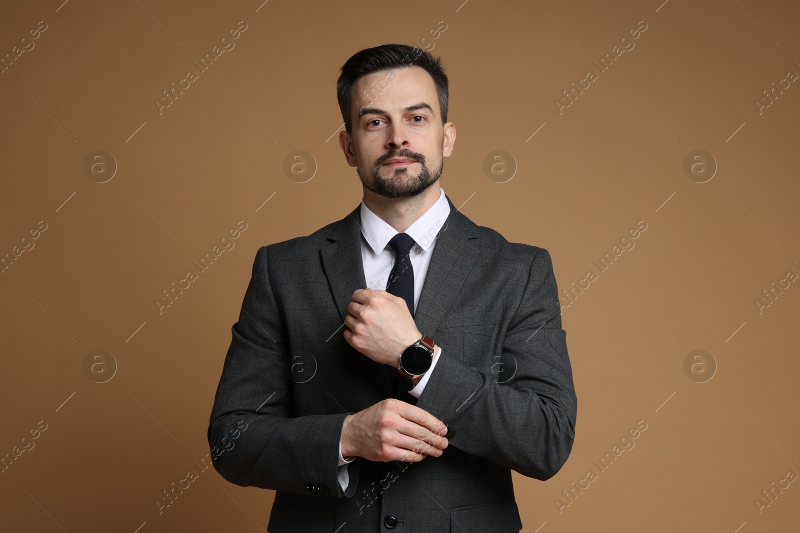 Photo of Confident man in classic suit with stylish watch on brown background