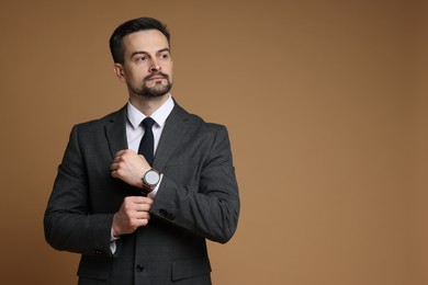 Photo of Confident man in classic suit with stylish watch on brown background. Space for text