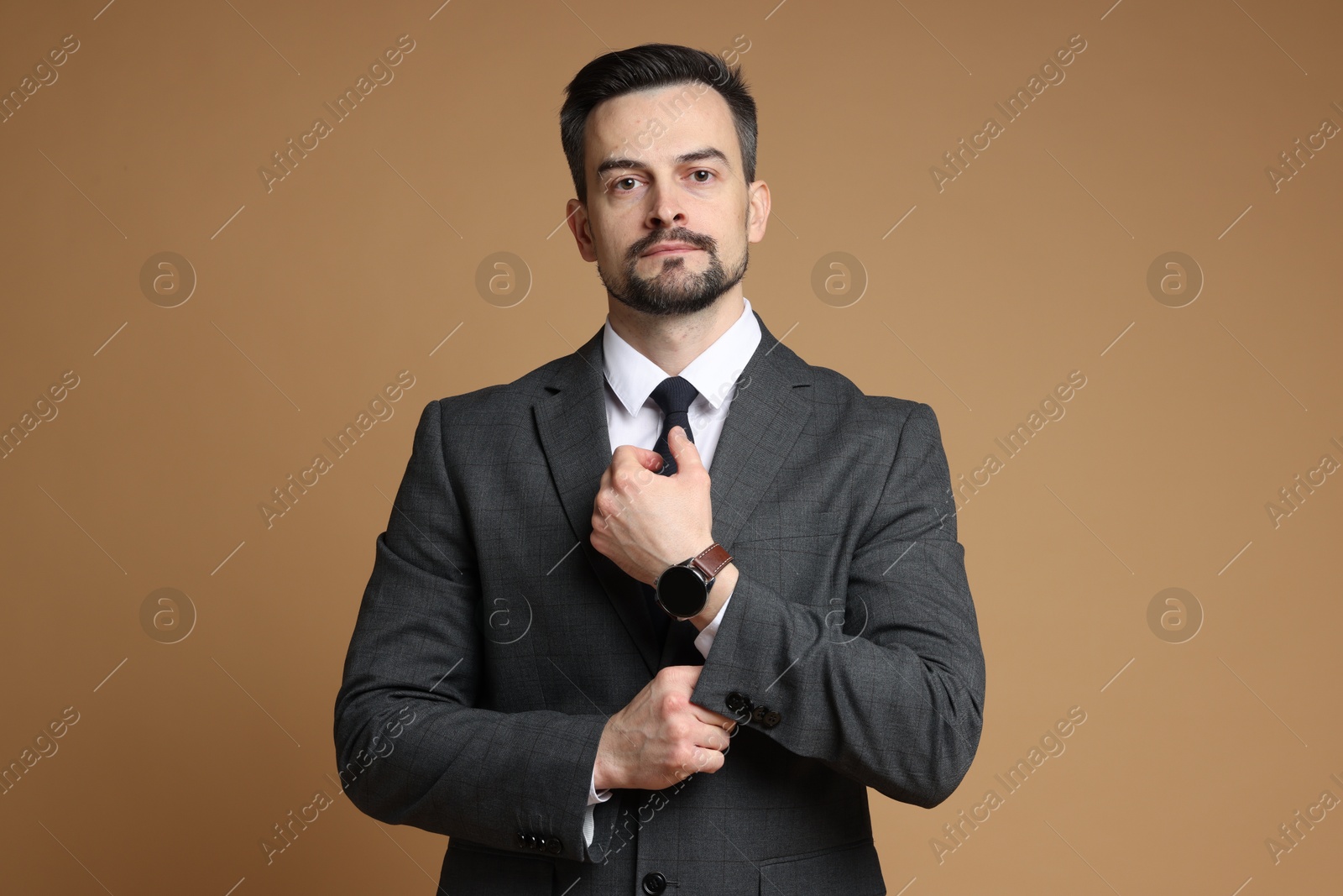 Photo of Confident man in classic suit with stylish watch on brown background