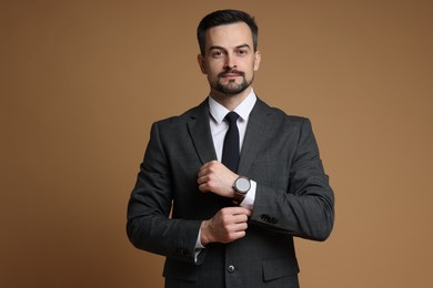 Photo of Confident man in classic suit with stylish watch on brown background