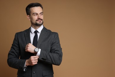 Photo of Confident man in classic suit with stylish watch on brown background. Space for text