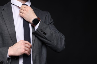 Photo of Man in classic suit straightening tie on black background, closeup. Space for text