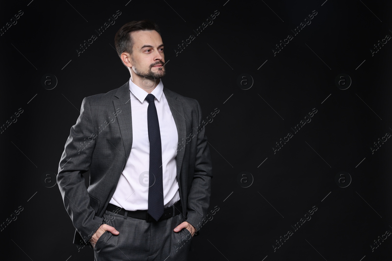 Photo of Confident man in classic suit on black background. Space for text