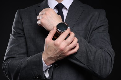 Photo of Man in classic suit with stylish watch on black background, closeup