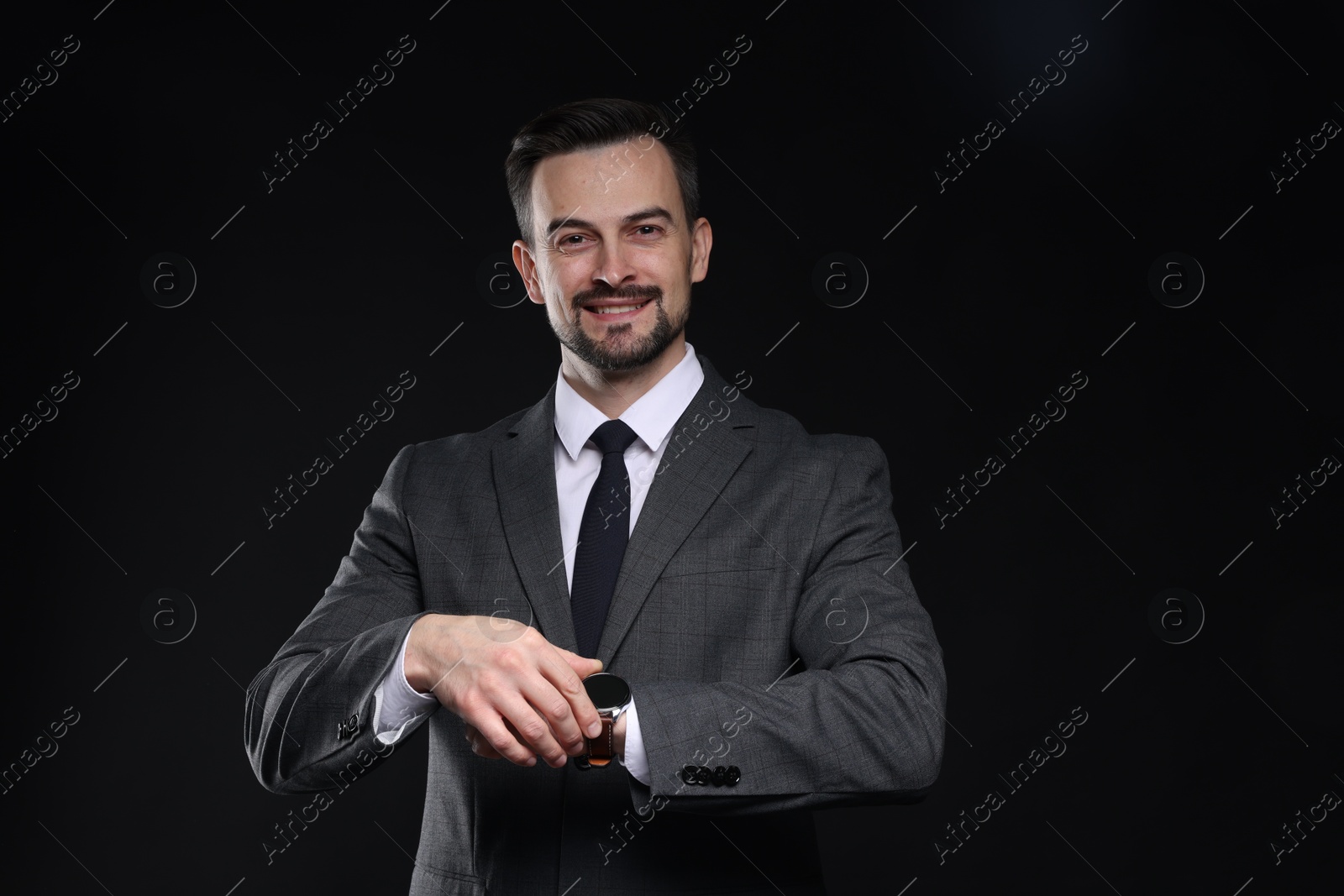 Photo of Handsome man in classic suit checking time on black background