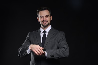 Photo of Handsome man in classic suit checking time on black background