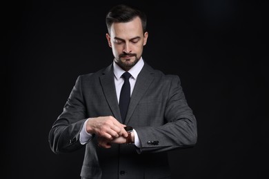 Photo of Handsome man in classic suit checking time on black background