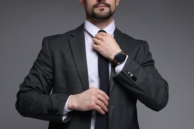 Photo of Man in classic suit straightening tie on grey background, closeup