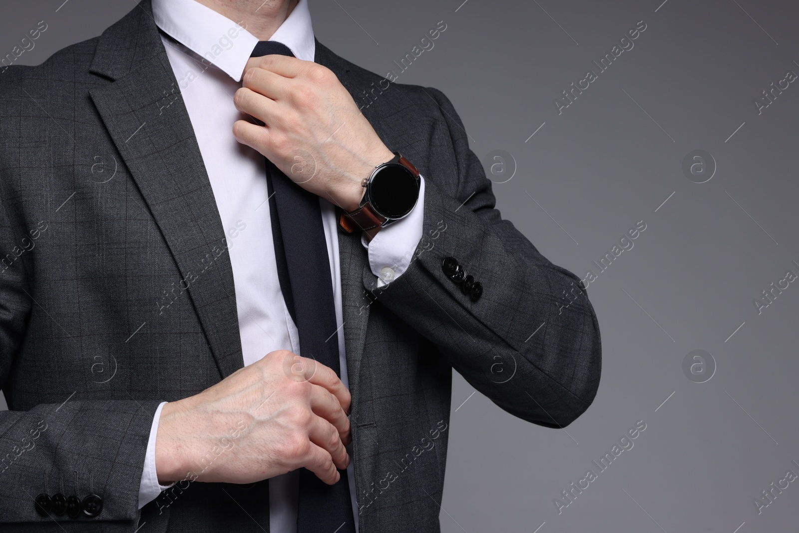 Photo of Confident man in classic suit straightening tie on grey background, closeup. Space for text