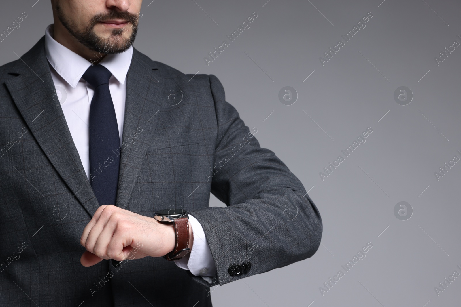 Photo of Man in classic suit checking time on grey background, closeup. Space for text