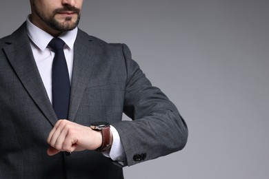 Photo of Man in classic suit checking time on grey background, closeup. Space for text