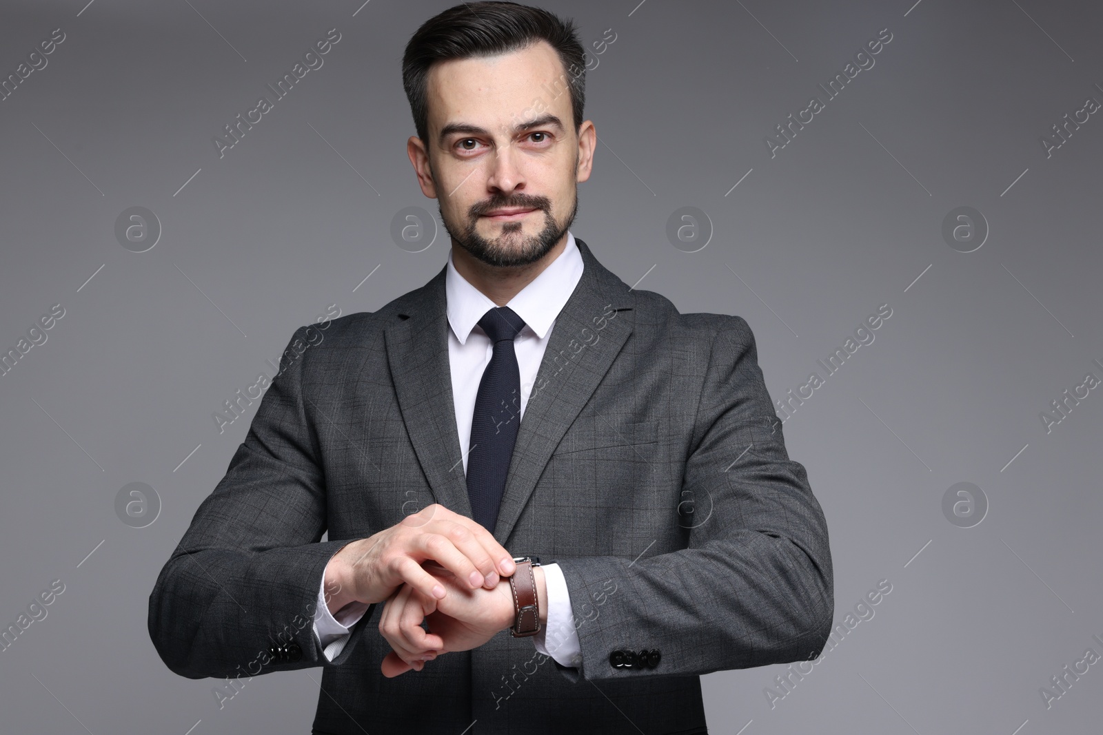 Photo of Confident man in classic suit checking time on grey background