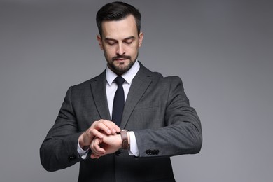 Photo of Confident man in classic suit checking time on grey background