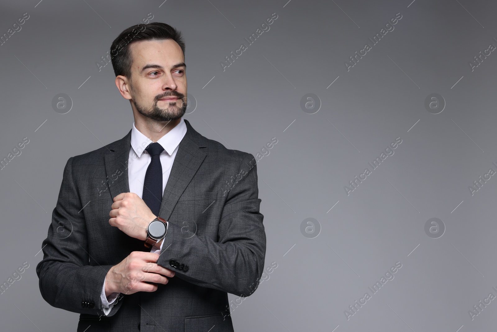 Photo of Handsome man in classic suit with stylish watch on grey background. Space for text