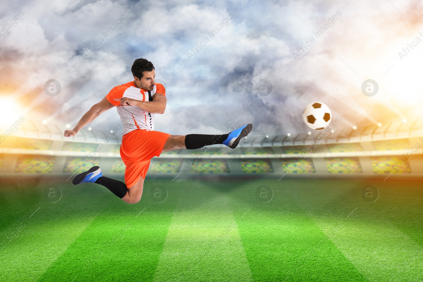 Image of Young man playing football under lights at stadium