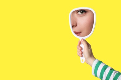 Image of Beautiful woman looking in handheld mirror on yellow background, closeup