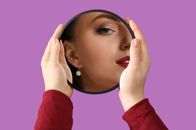 Image of Beautiful woman looking in small round mirror on violet background, closeup