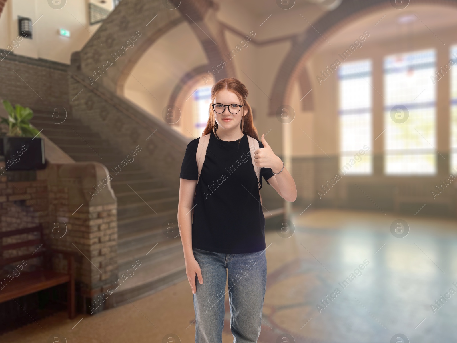 Image of Teenage student with eyeglasses and backpack showing thumbs-up gesture in college