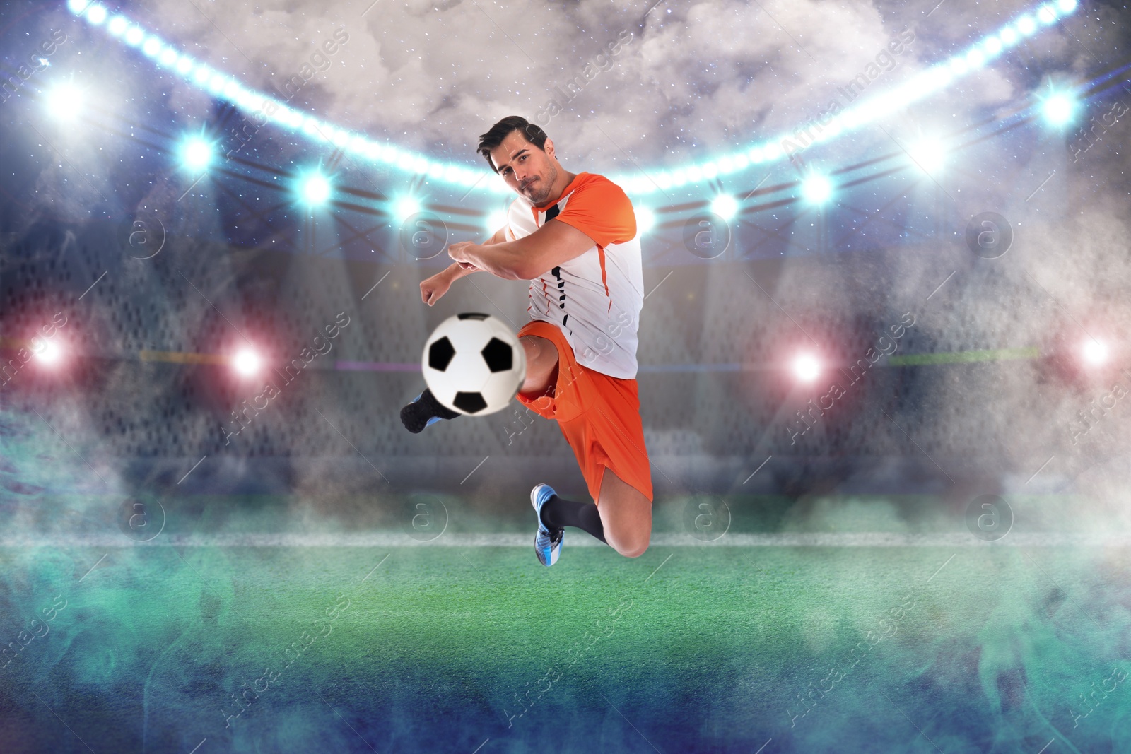 Image of Young man playing football under lights at stadium