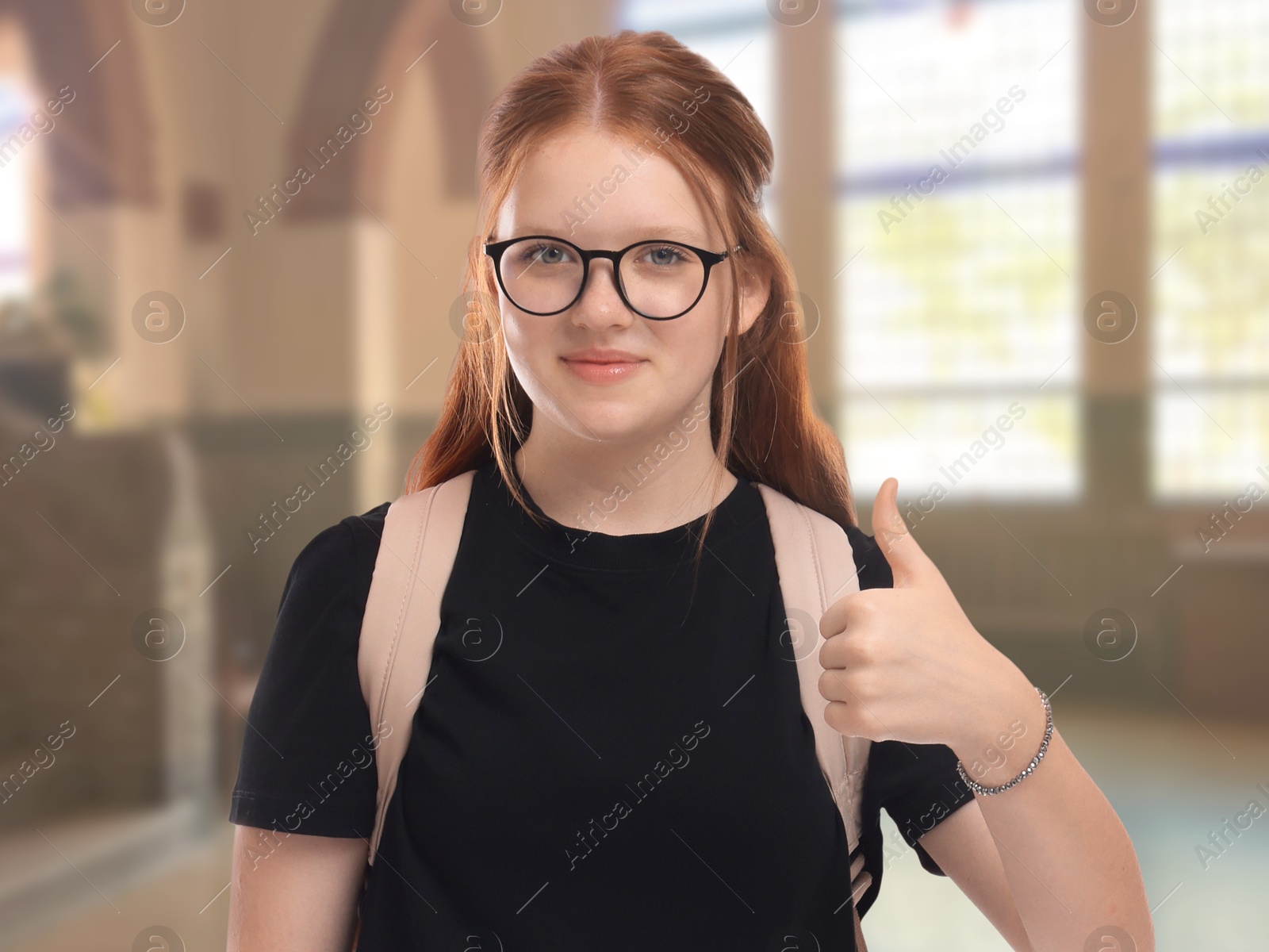 Image of Teenage student with eyeglasses and backpack showing thumbs-up gesture in college