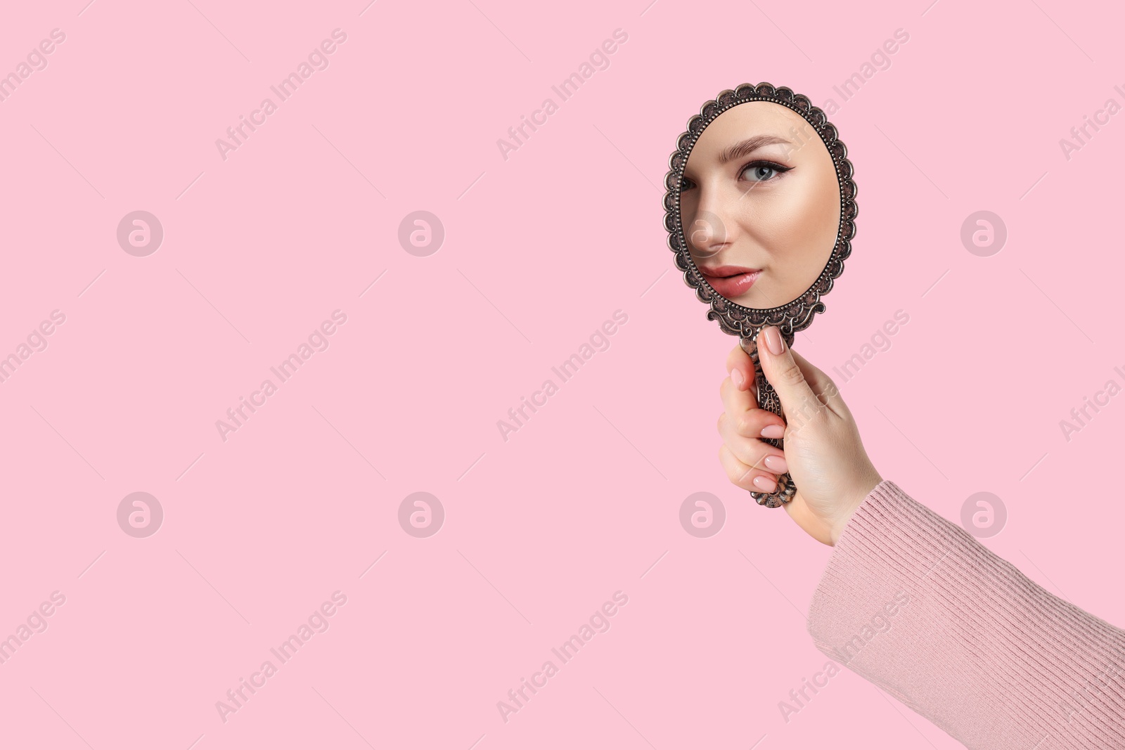 Image of Beautiful woman looking in handheld mirror on pink background, closeup. Space for text