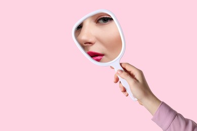 Image of Beautiful woman looking in handheld mirror on pink background, closeup