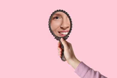 Image of Beautiful woman looking in handheld mirror on pink background, closeup