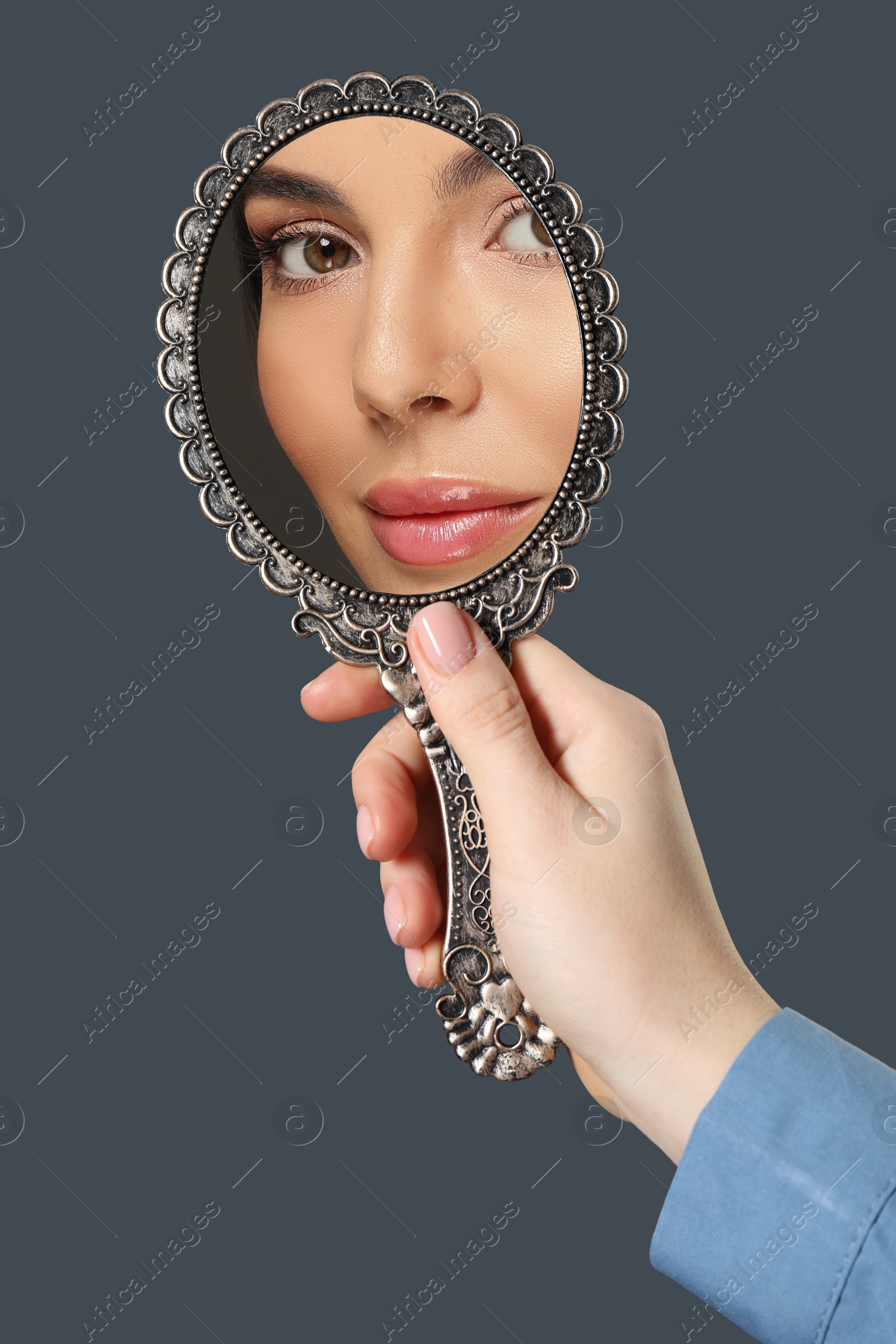 Image of Beautiful woman looking in handheld mirror on dark grey background, closeup