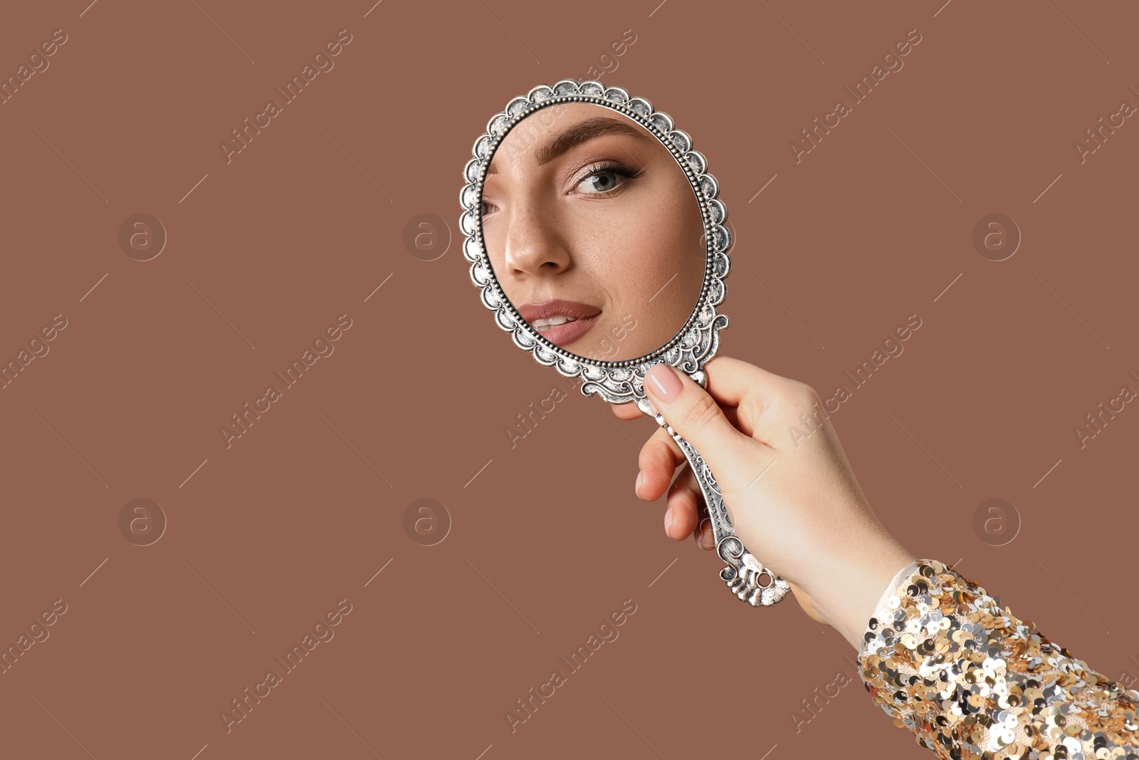 Image of Beautiful woman looking in handheld mirror on brown background, closeup