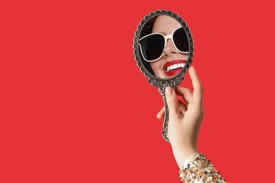 Image of Beautiful woman looking in handheld mirror on red background, closeup