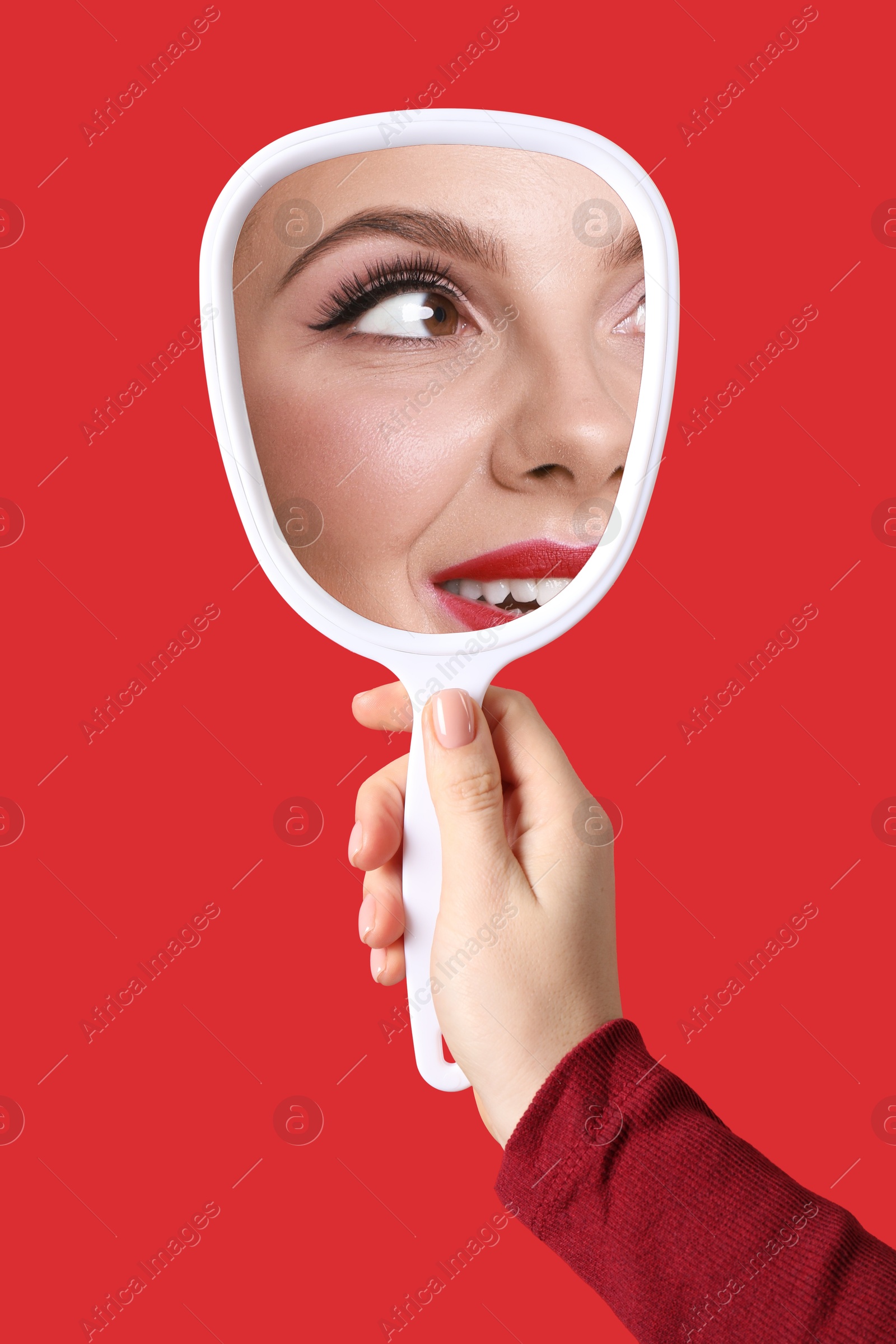 Image of Beautiful woman looking in handheld mirror on red background, closeup