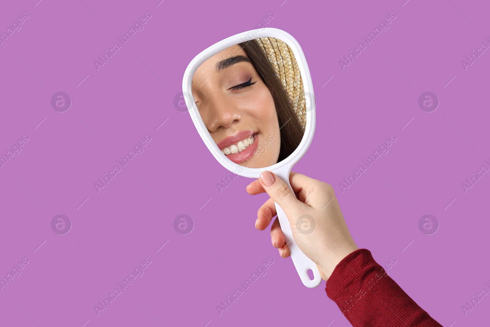 Image of Beautiful woman looking in handheld mirror on violet background, closeup